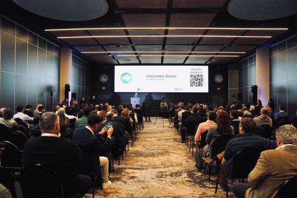 Público sentado en una conferencia; la pantalla muestra a Alejandro Bravo y un código QR para preguntas