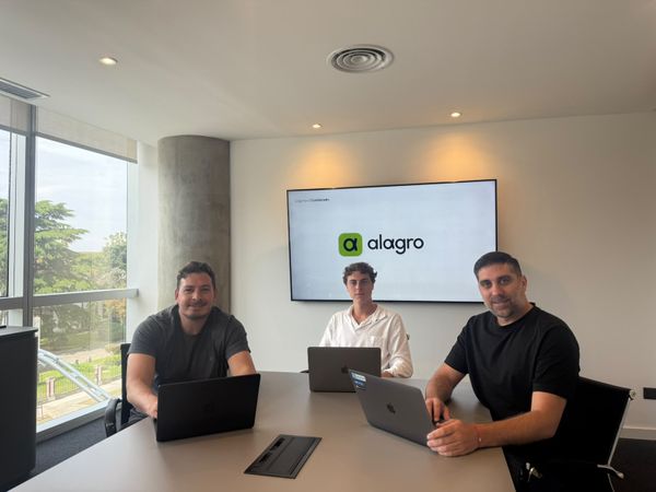 Tres integrantes de Alagro trabajando con sus notebooks en una sala de reuniones, frente a una pantalla con el logo de la plataforma