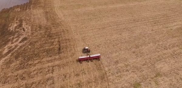 Vista aérea de un tractor rojo y un equipo sembradora de color rojo avanzando por un lote de tierra arada en un campo agrícola