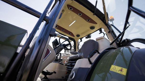 Interior de cabina de tractor con volante, asiento con suspensión y consola de mandos, visto desde la puerta abierta