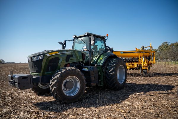 Tractor verde con sembradora amarilla montada en un lote con rastrojo, listo para la siembra