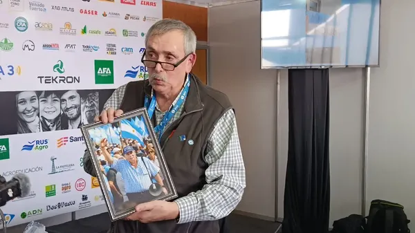 Hombre de anteojos sostiene un portarretrato con una foto de un hombre entre banderas argentinas