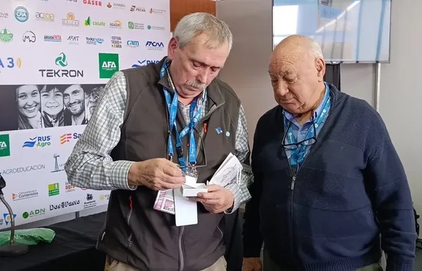 Dos hombres mayores con credenciales revisan papeles en un evento del sector agropecuario