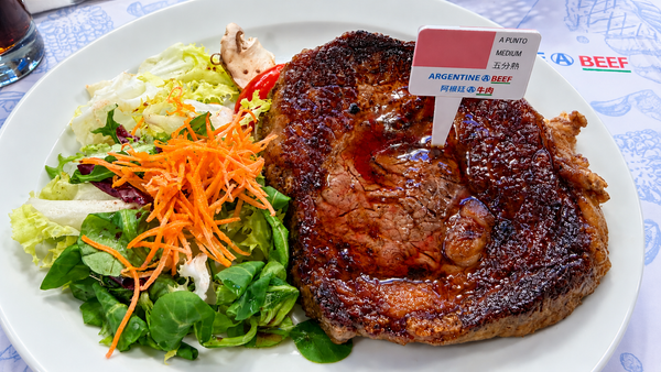 Bife de chorizo a punto medium con ensalada verde y zanahoria, con cartel de "Argentine Beef