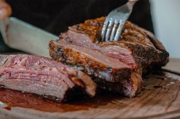 Carne vacuna asada cortada en tajadas sobre tabla de madera, con un tenedor clavado en el corte