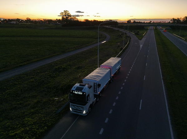 Camión con acoplado tipo bitren circulando por una ruta de doble vía al atardecer, con campos a un costado.