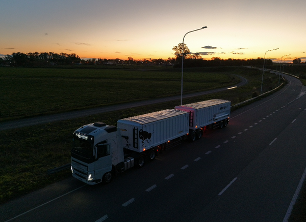 Camión con dos acoplados tipo bitren en una ruta al atardecer, con cajas cerradas blancas y un tubo de descarga lateral