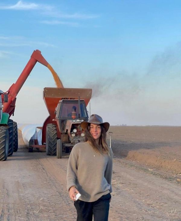 Mujer con sombrero junto a un tractor que descarga granos en la cosecha, en un camino rural
