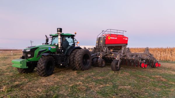 Tractor verde con sembradora Indecar roja enganchada, en un campo