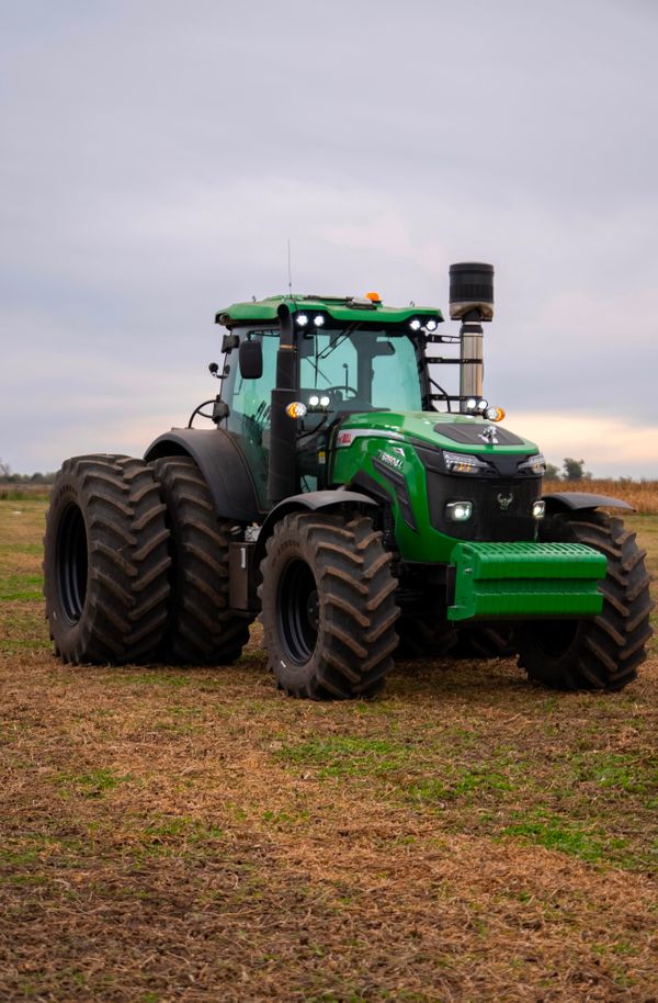 Tractor verde de gran porte con neumáticos dobles, estacionado en un campo con rastrojo; se ve el logo de la marca en el capó.